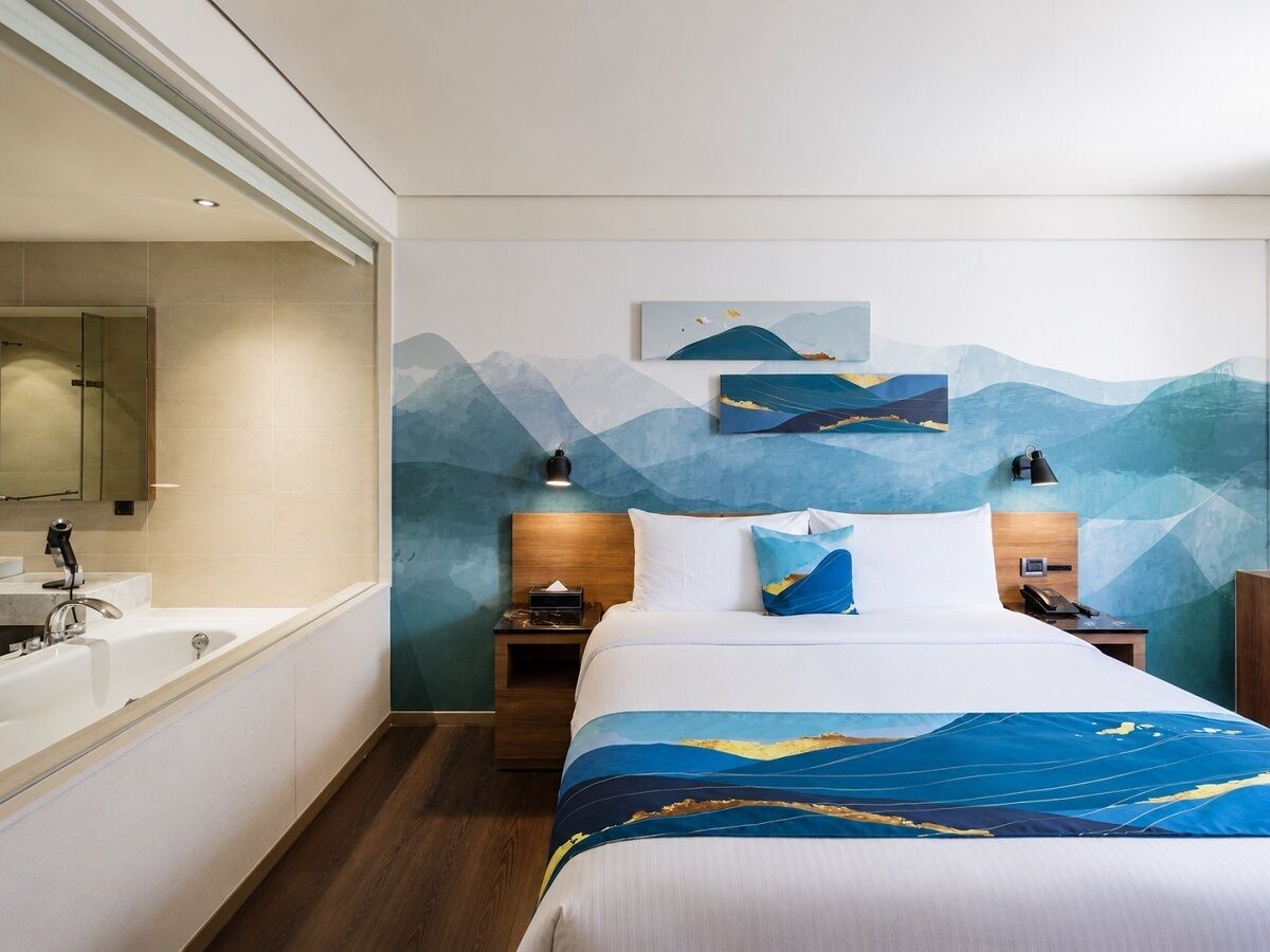 A hotel room with a large bed, a bathroom with a bathtub, and a wall with a mountain landscape painting.