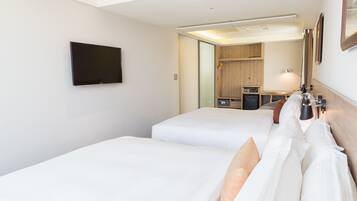 A hotel room with two beds, a TV mounted on the wall, a desk with a lamp, and a mirror.