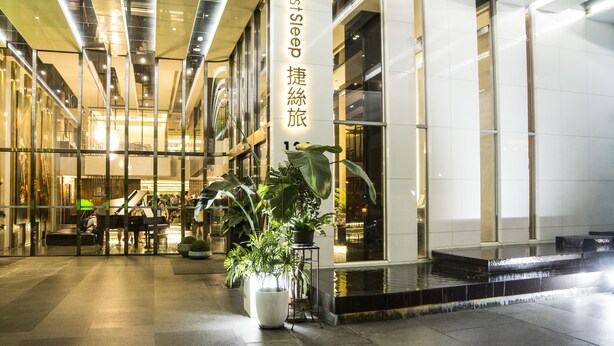 Un hall d’hôtel moderne, agrémenté d’un grand piano, de grands pots de plantes et d’une enseigne indiquant : « Dormez bien. »