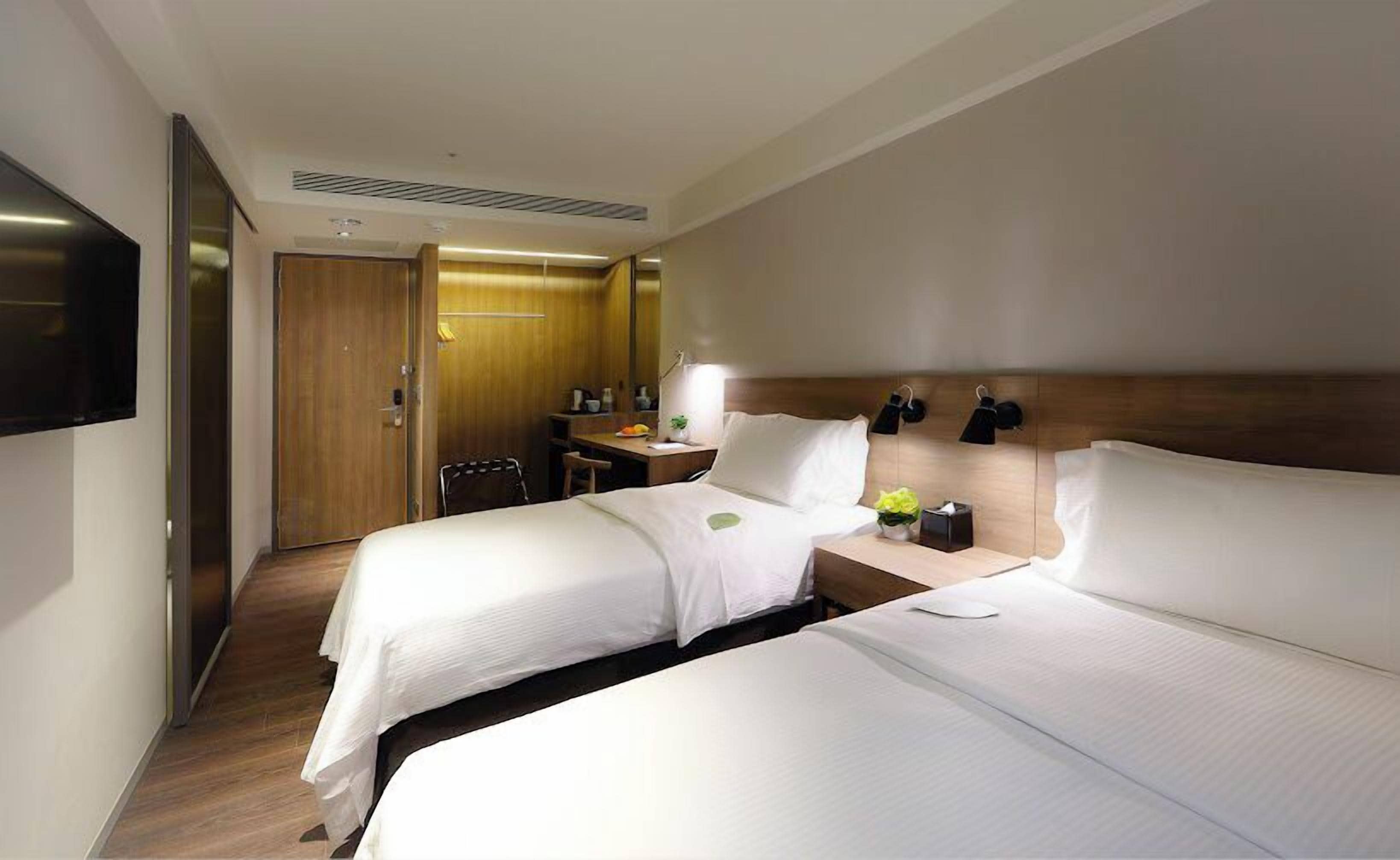 A hotel room with two beds, a desk, a chair, a television, and a mirror.