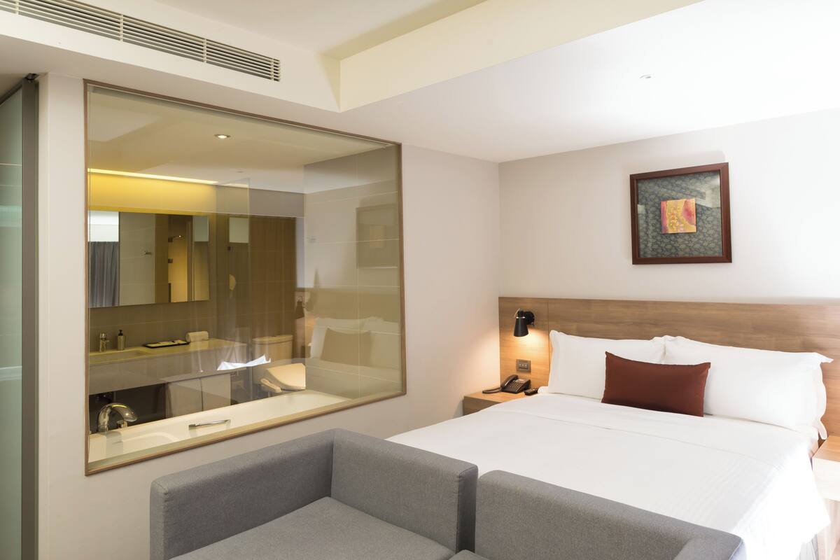 Una camera d'albergo con un letto grande, un comodino con una lampada, uno specchio ampio e un quadro appeso alla parete.
