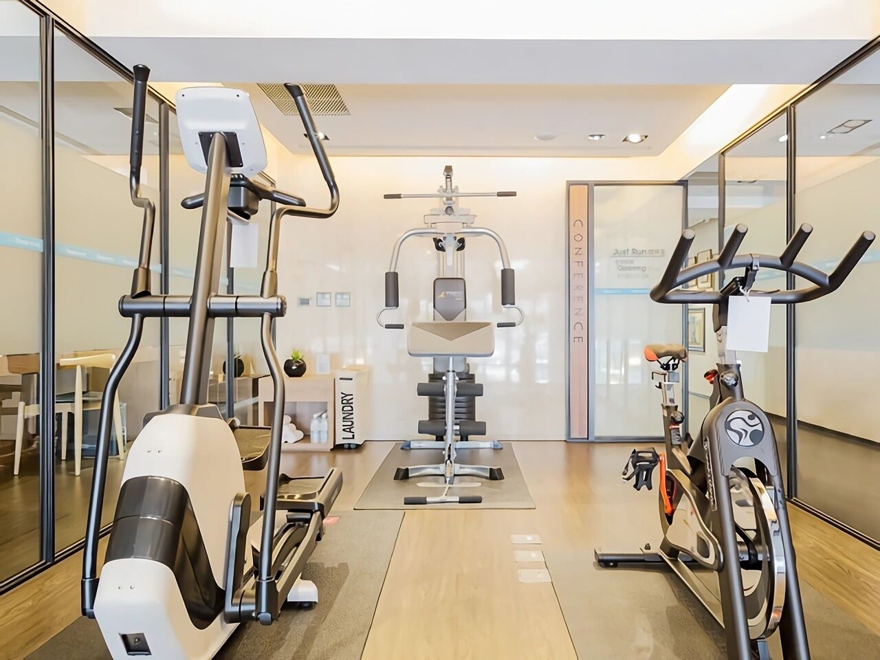 Un gimnasio moderno con máquinas de cardio, equipo de entrenamiento con pesas y un espejo grande.