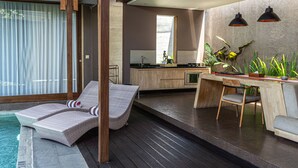 A modern kitchen with a bar area, a dining table, and a poolside lounge area with a chair and a small table. - Asa Bali Luxury Villas & Spa (Seminyak)