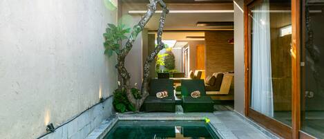 A pool area with a floating basket of food, lounge chairs, and a tree.