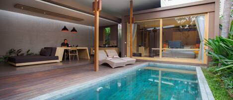 Un área de piscina moderna al aire libre con sillones de descanso, una terraza de madera y un comedor con paredes de cristal.
