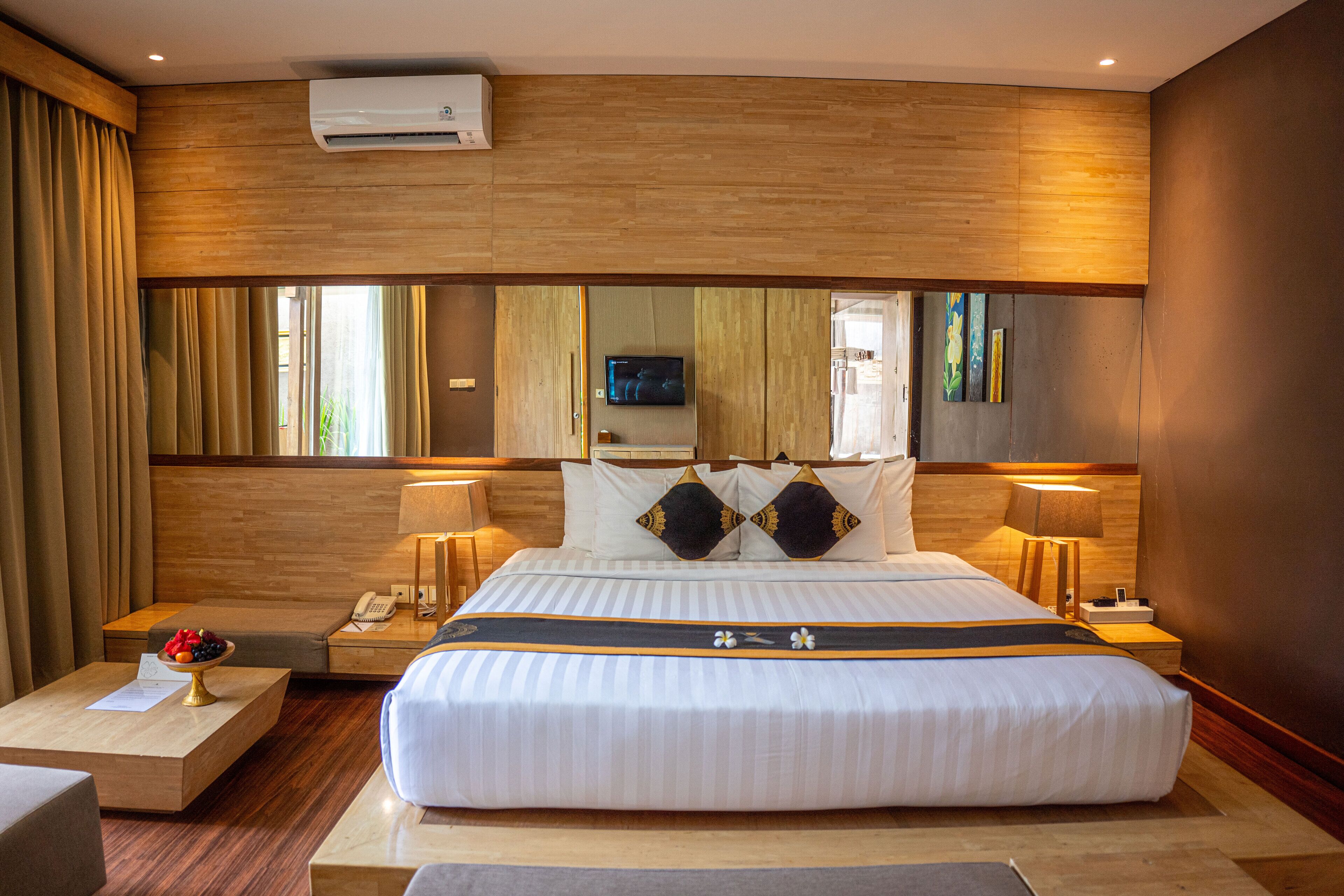 A hotel room with a large bed, two bedside tables with lamps, a flat-screen TV, and a wooden headboard.