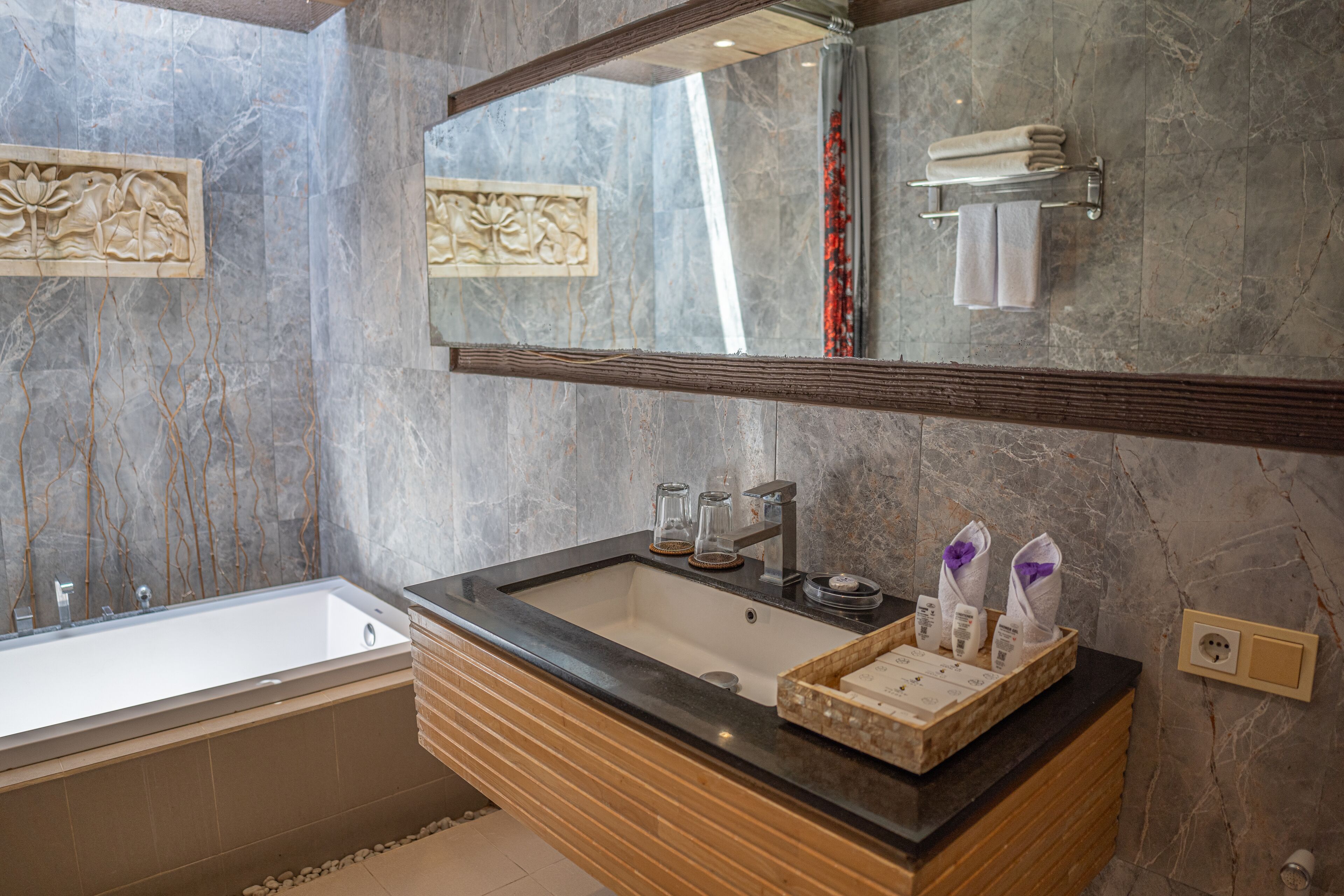 A modern bathroom with a large bathtub, a vanity with a black countertop, and a mirror above the sink.
