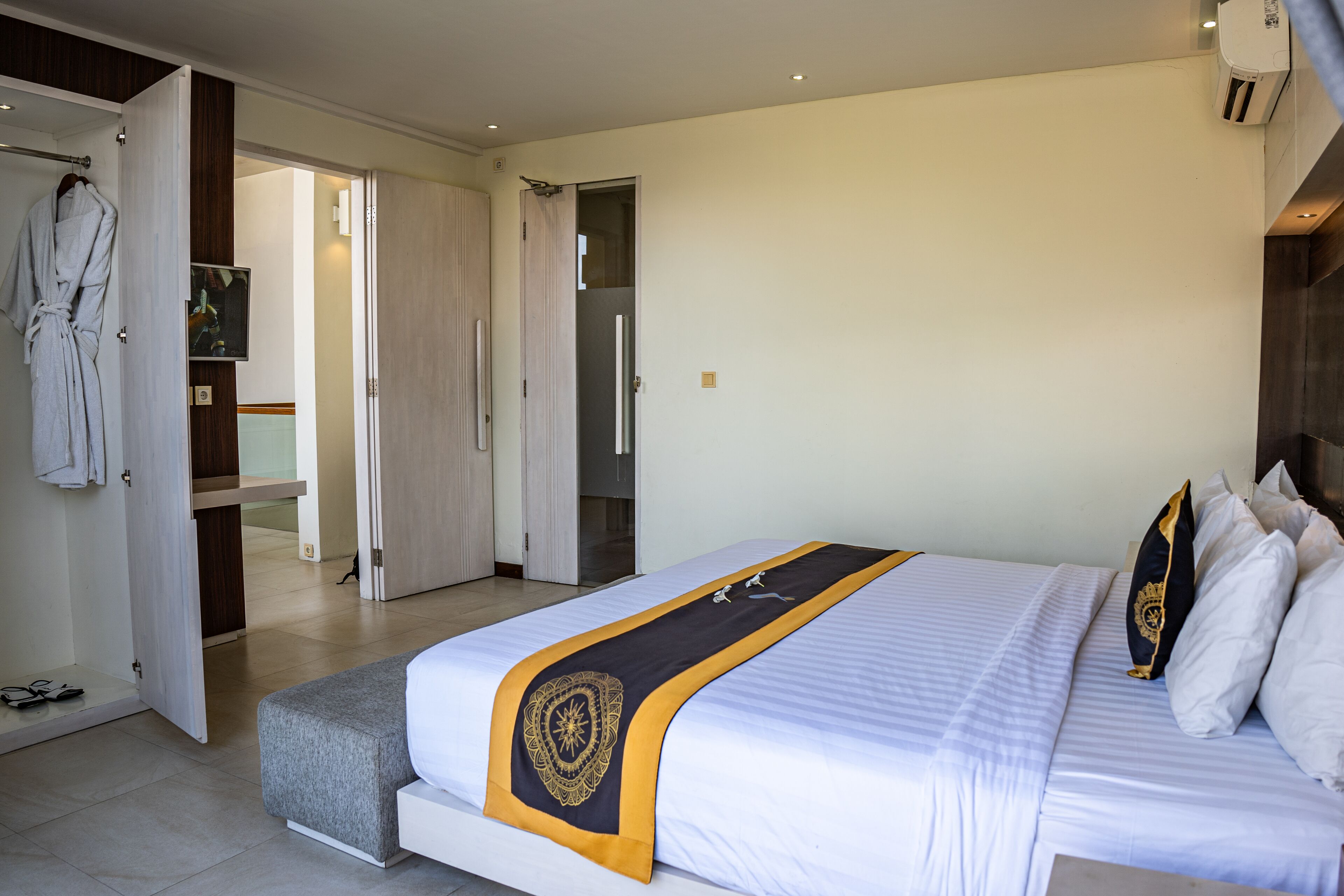 A hotel room with a large bed, a robe hanging on a door, and a bathroom visible through an open door.