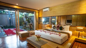 A modern bedroom with a large bed, a wooden floor, a glass door leading to a garden, and a television on the wall.