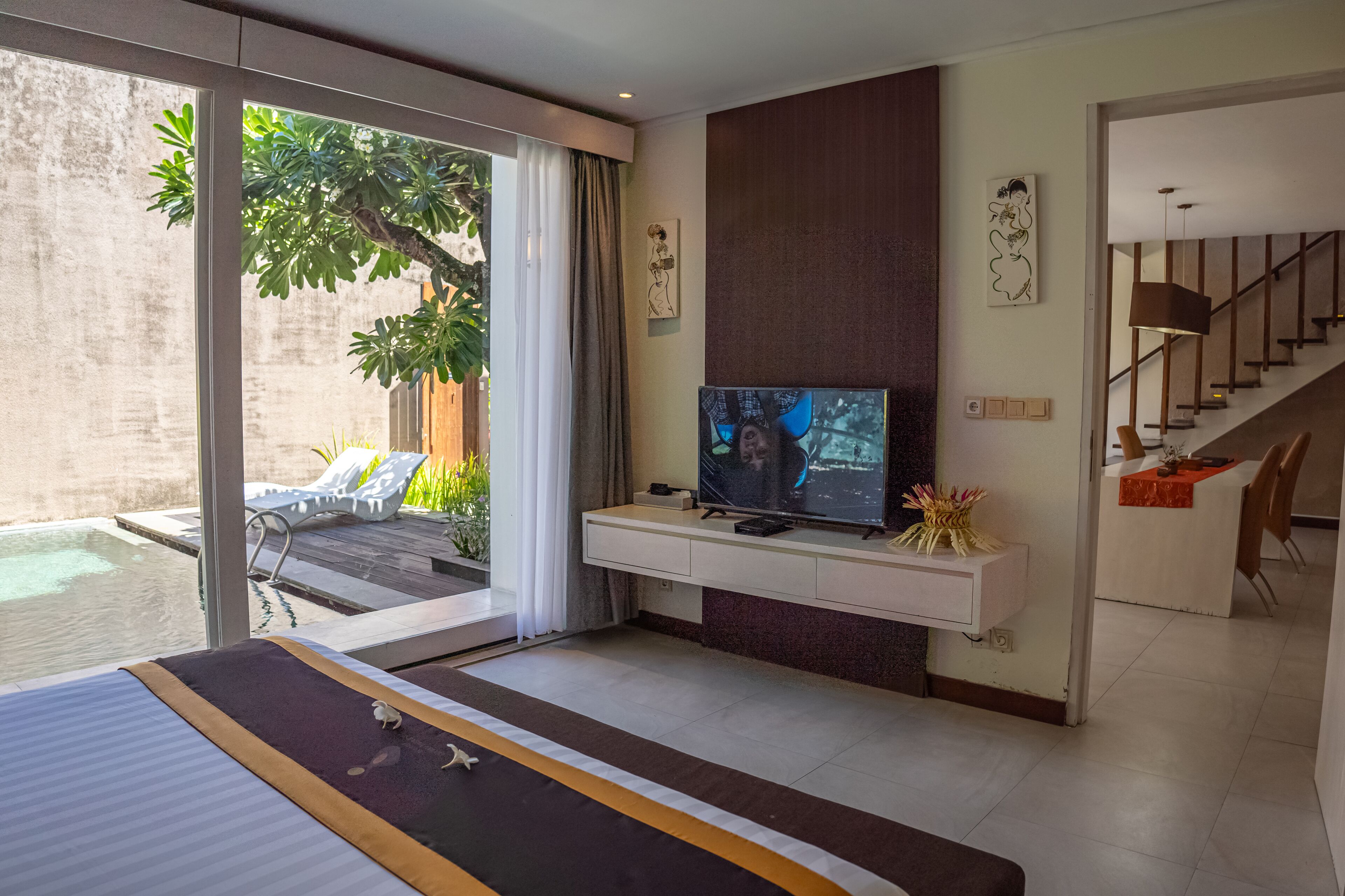 Una habitación de hotel moderna con una cama grande, televisor, puerta corrediza de vidrio que da a una piscina y una escalera al piso superior.