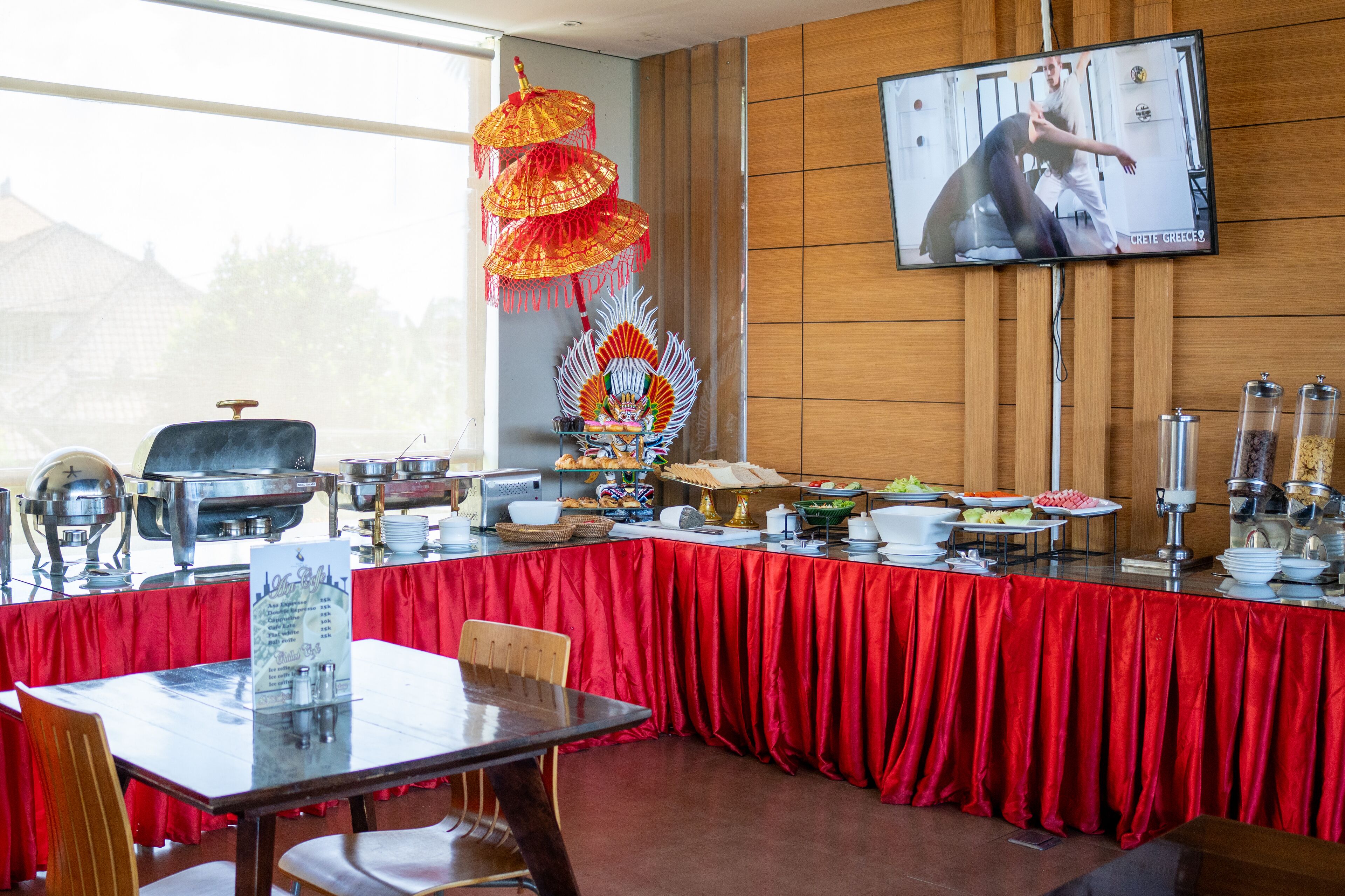 A buffet setup with a red tablecloth, a television screen, and various food items.