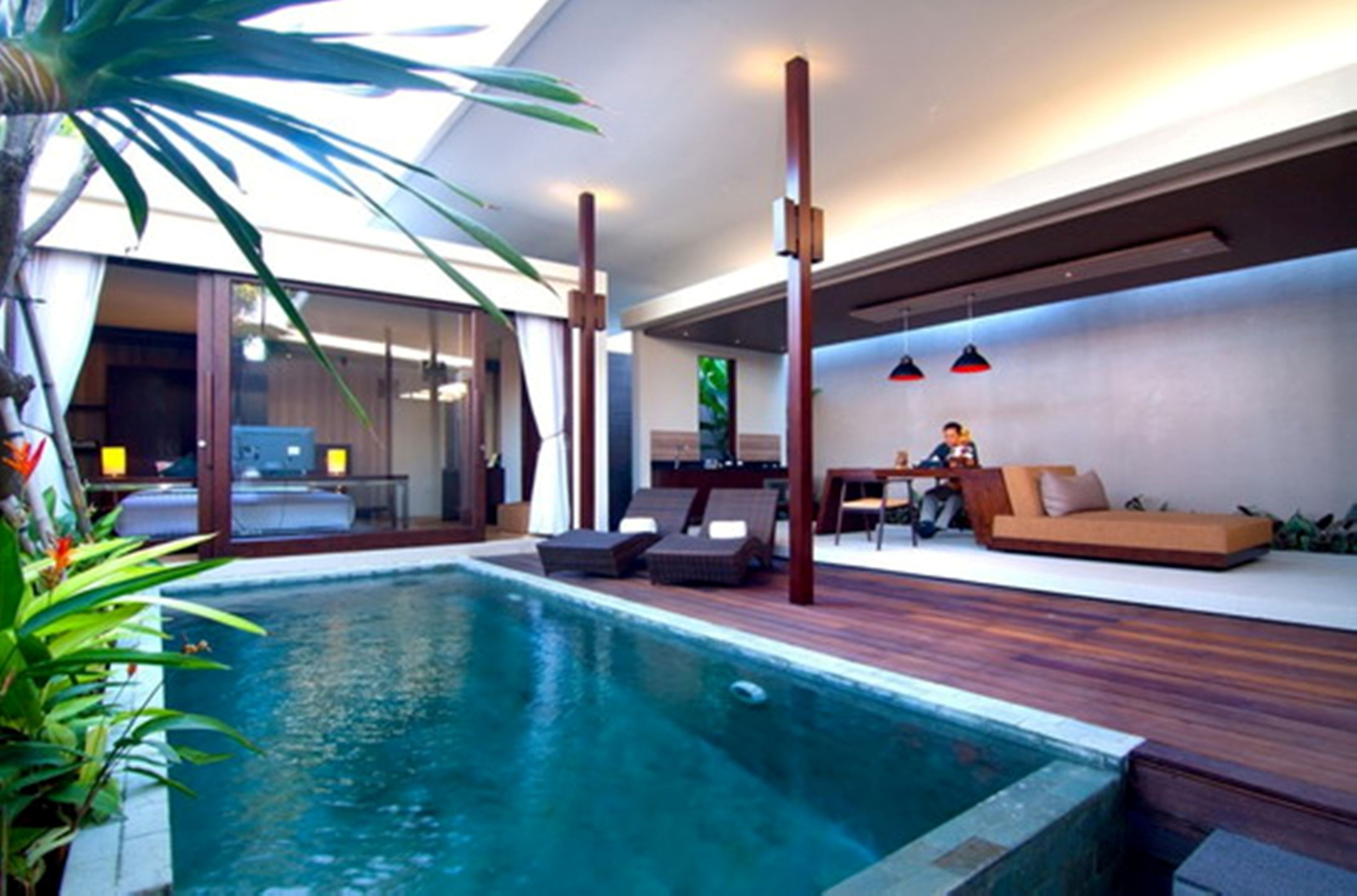 A modern indoor pool area with a wooden deck, lounge chairs, and a sofa.