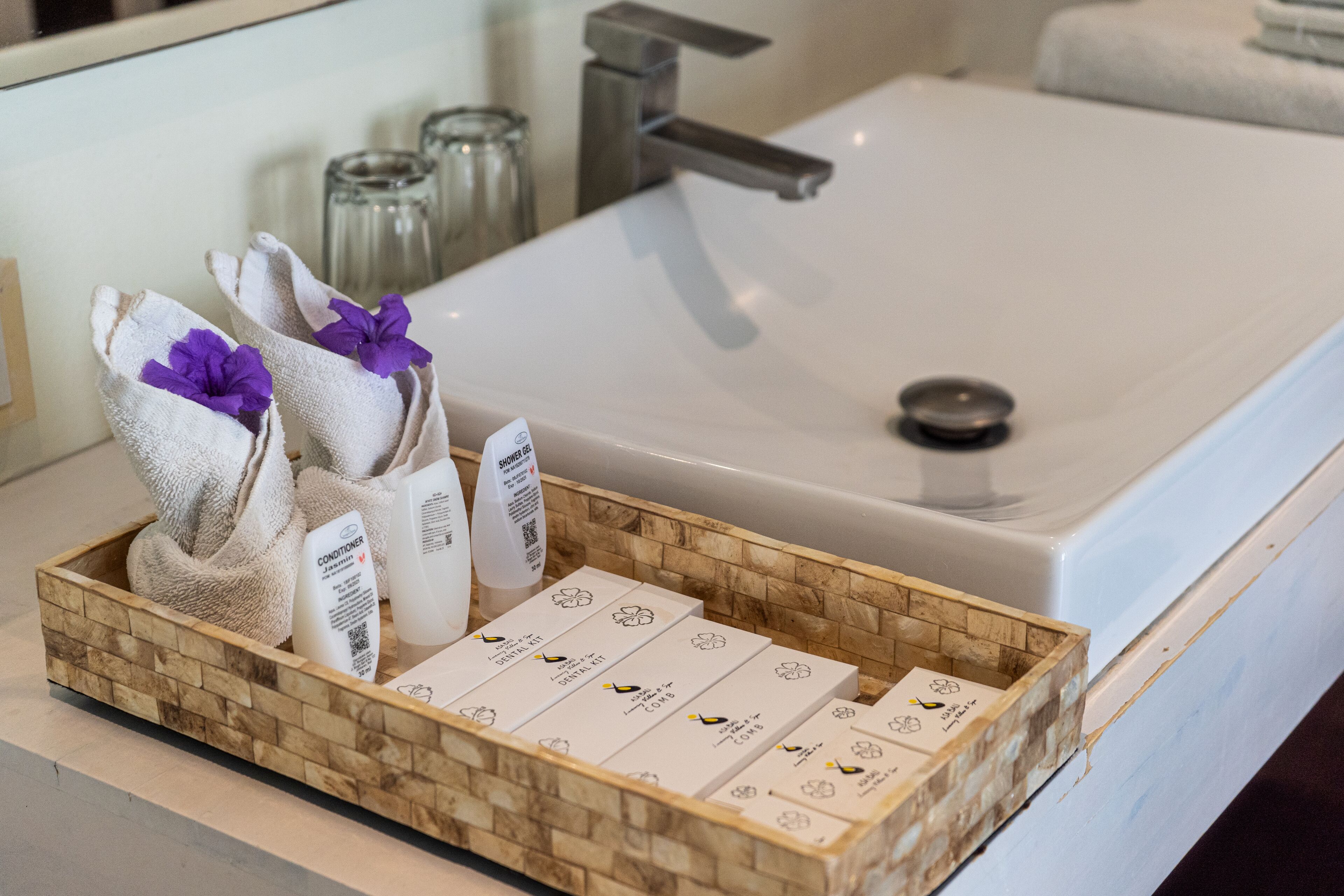 Une salle de bain avec un lavabo blanc, un plateau en bois contenant des articles de toilette et un miroir.