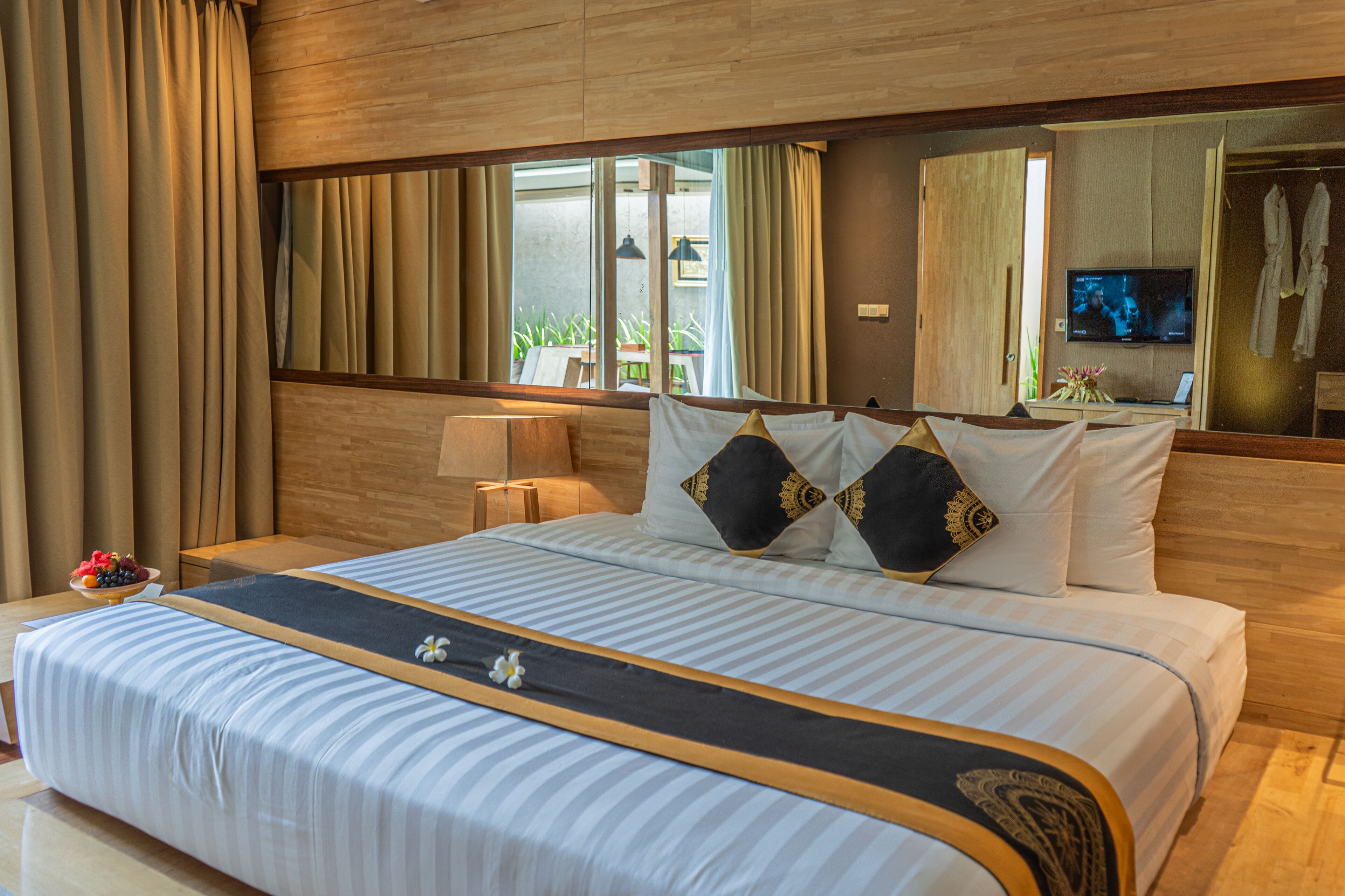 A hotel room with a large bed, wooden headboard, and a television on the wall.