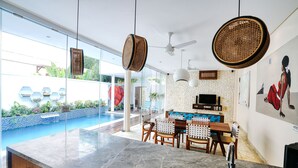 Una cocina moderna con encimera de mármol, sillas de madera y una mesa de comedor. Se observa un ventanal con vistas a una piscina y un jardín.