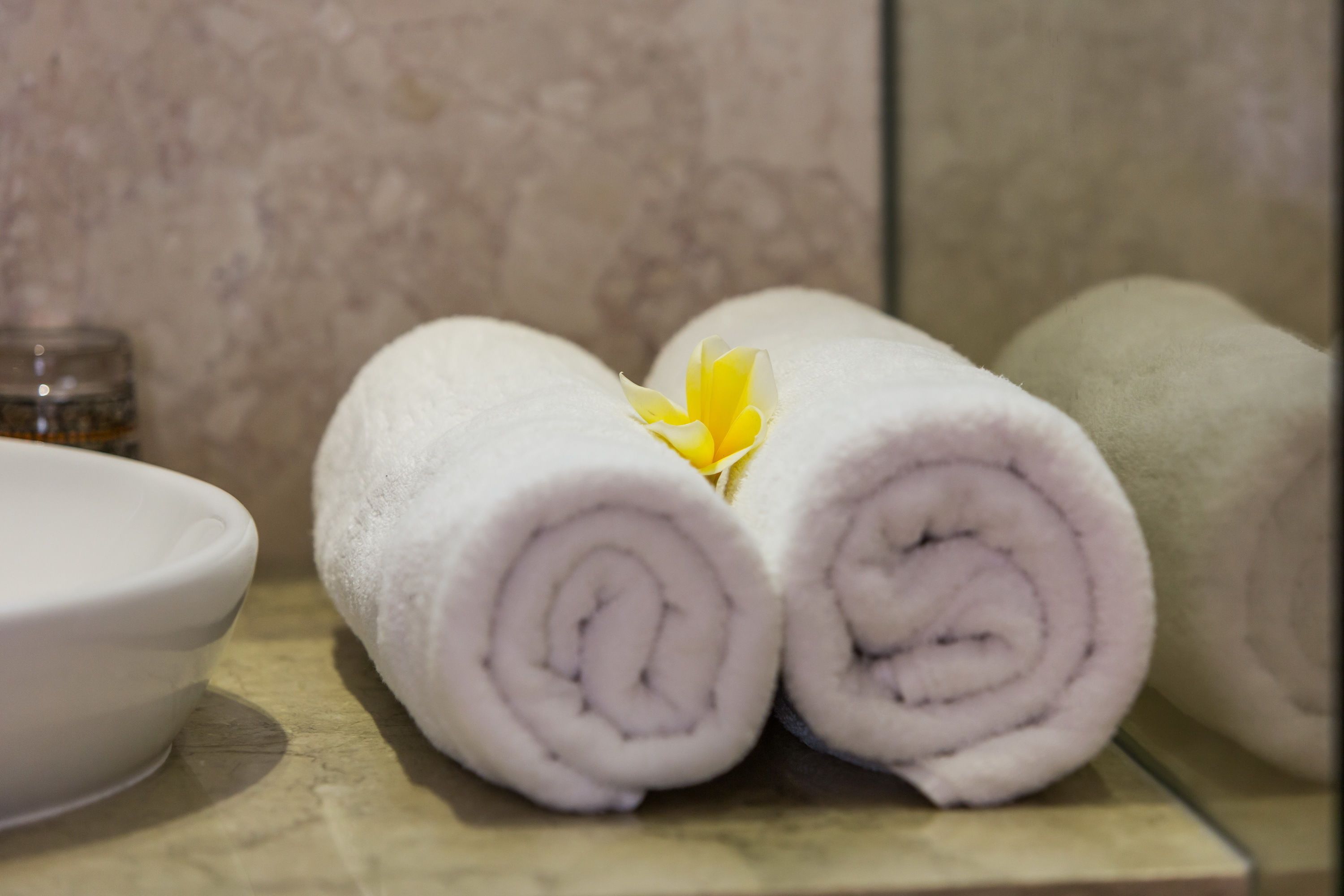Two rolled towels with a yellow flower in the center, placed on a textured surface.