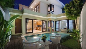 Una casa moderna con piscina, mobiliario de exterior e interiores bien iluminados.