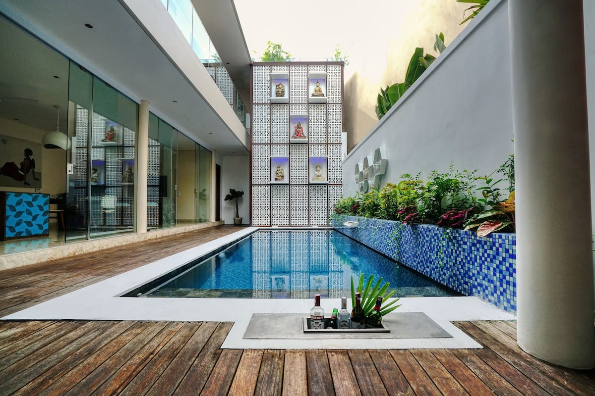 A modern indoor pool area with a wooden deck, a tiled blue wall, and a series of statues.
