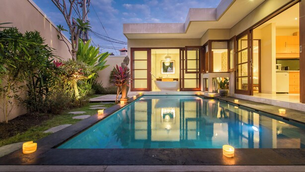 Una casa moderna con piscina, interior luminoso y jardín con plantas y una estatua.