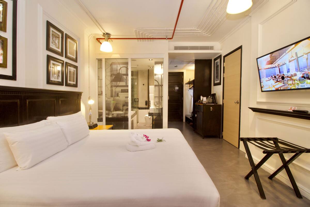 A hotel room with a large bed, a television, and a bathroom visible through a glass door.