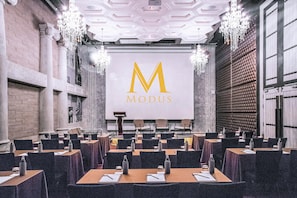 A conference room with a large screen displaying the logo "MODUS" in gold letters, surrounded by tables with chairs, water bottles, and notepads. - Pattaya Modus Beachfront Resort (Pattaya)