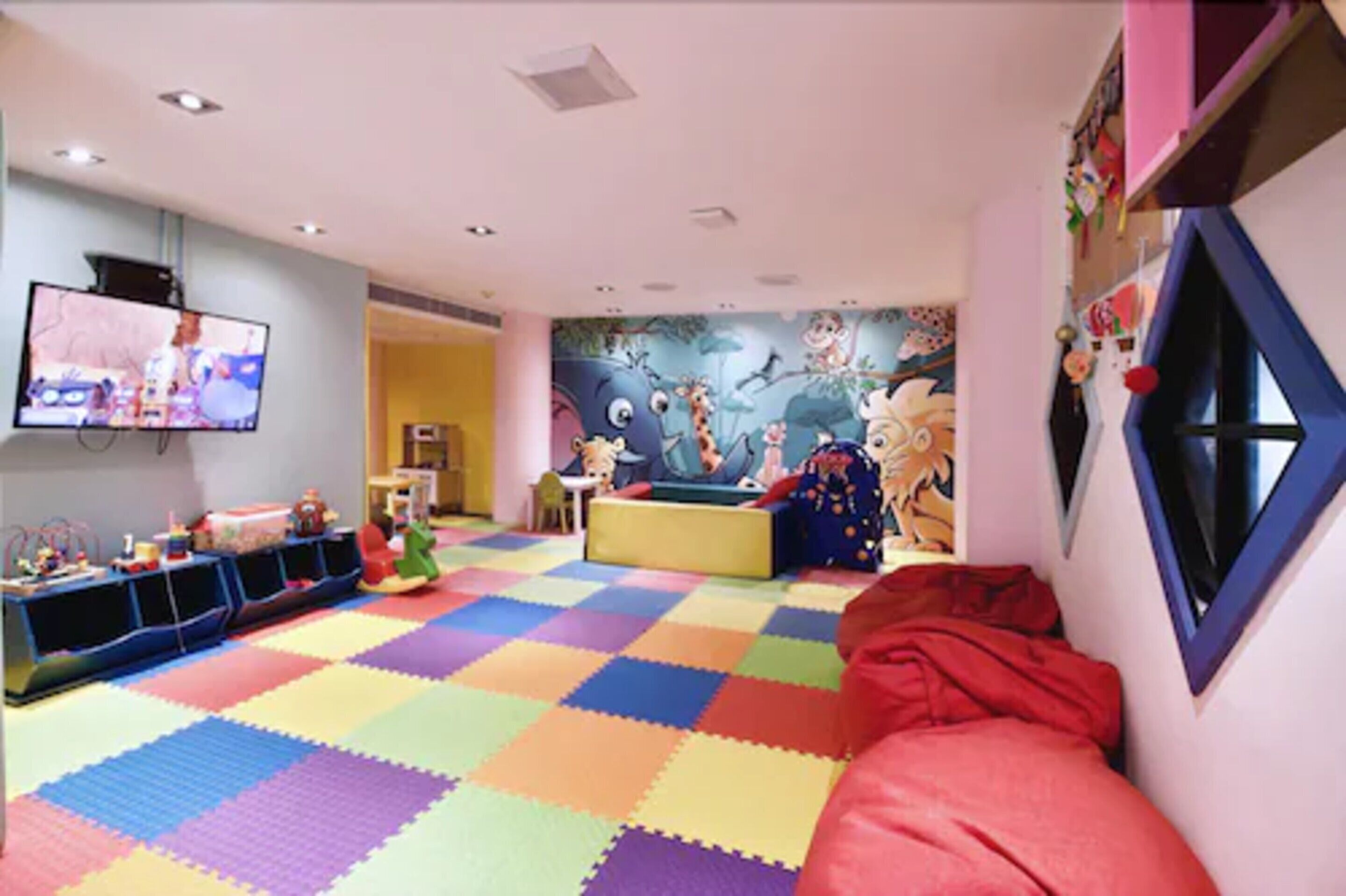 A children's playroom with a colorful foam floor, a television, and a mural on the wall.