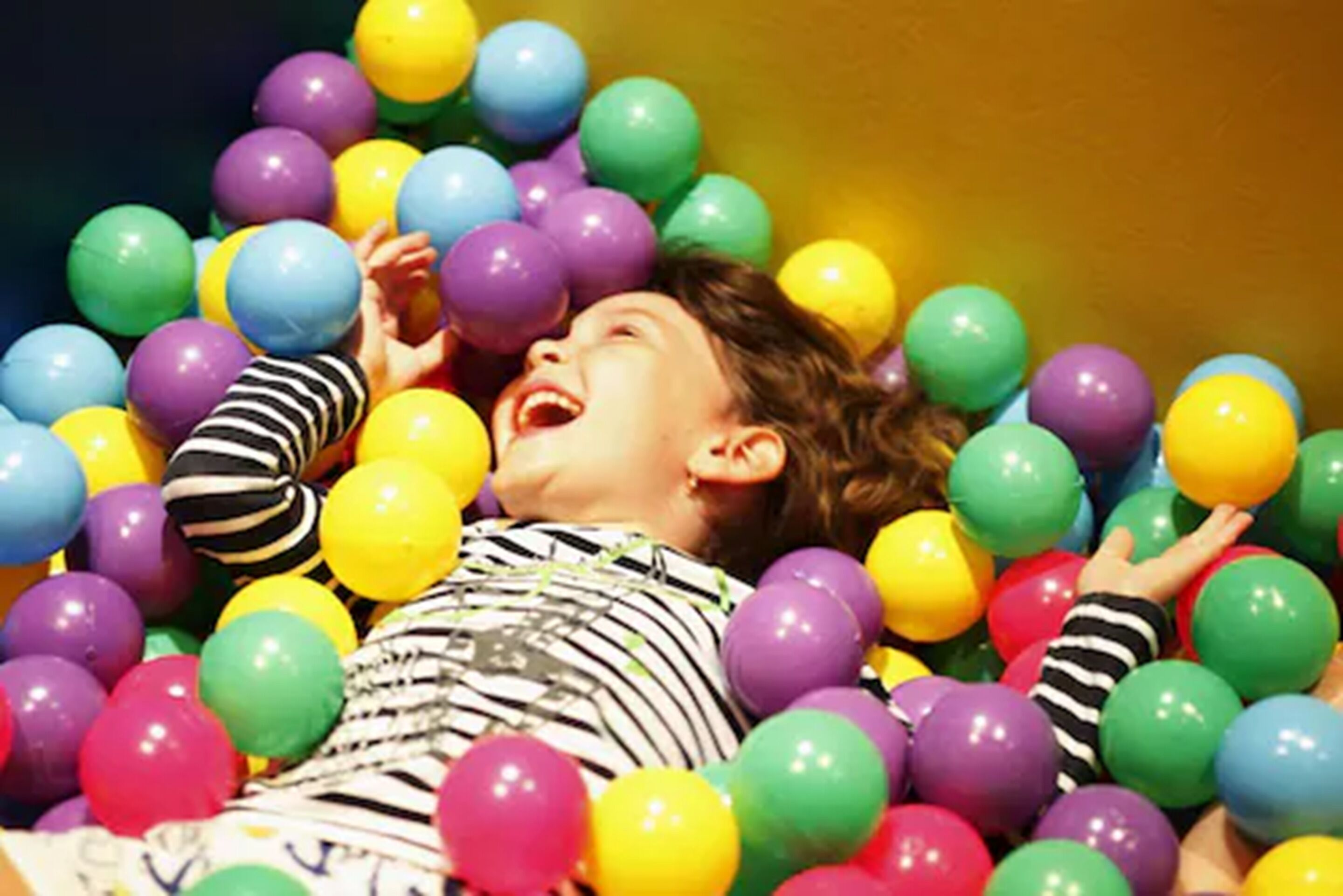 A child surrounded by colorful balloons in a room.