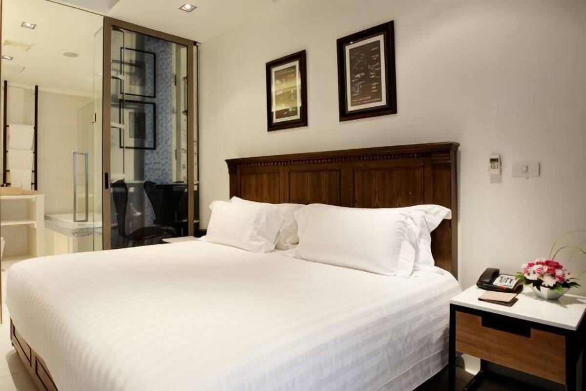 A hotel room with a large bed, a wooden headboard, a bedside table with a phone and a book, and two framed pictures on the wall.