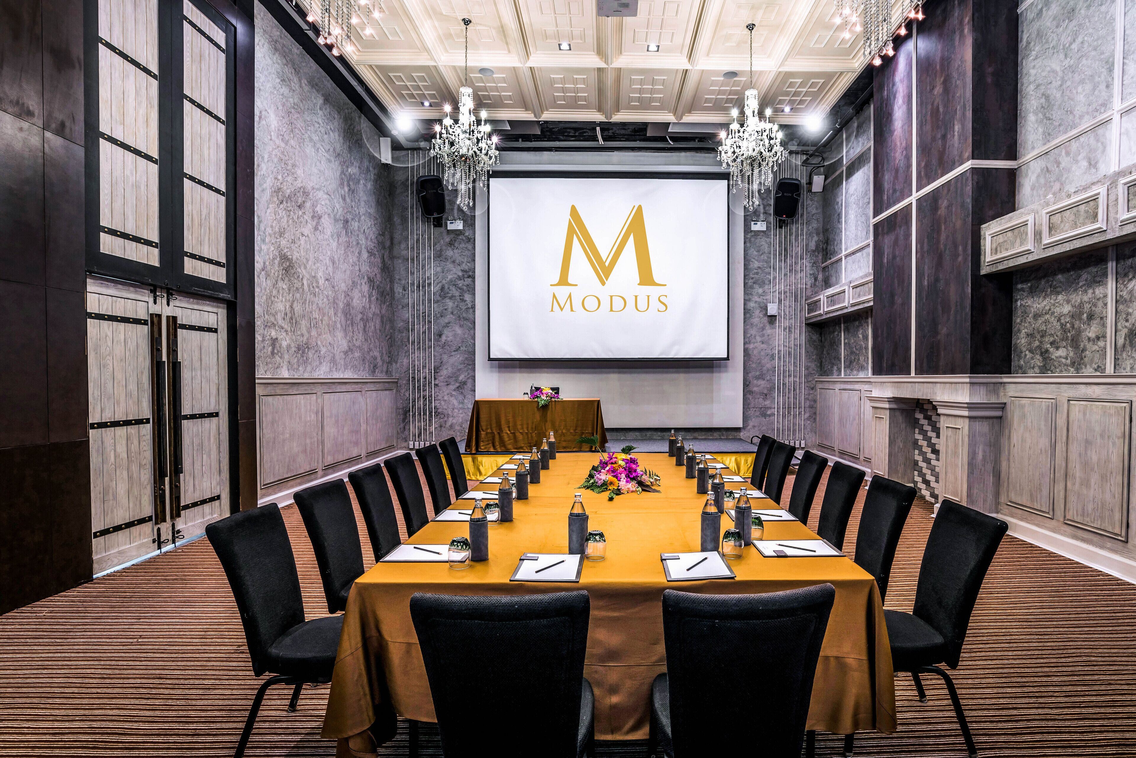 A conference room with a long table, black chairs, and a large screen displaying the MODUS logo.