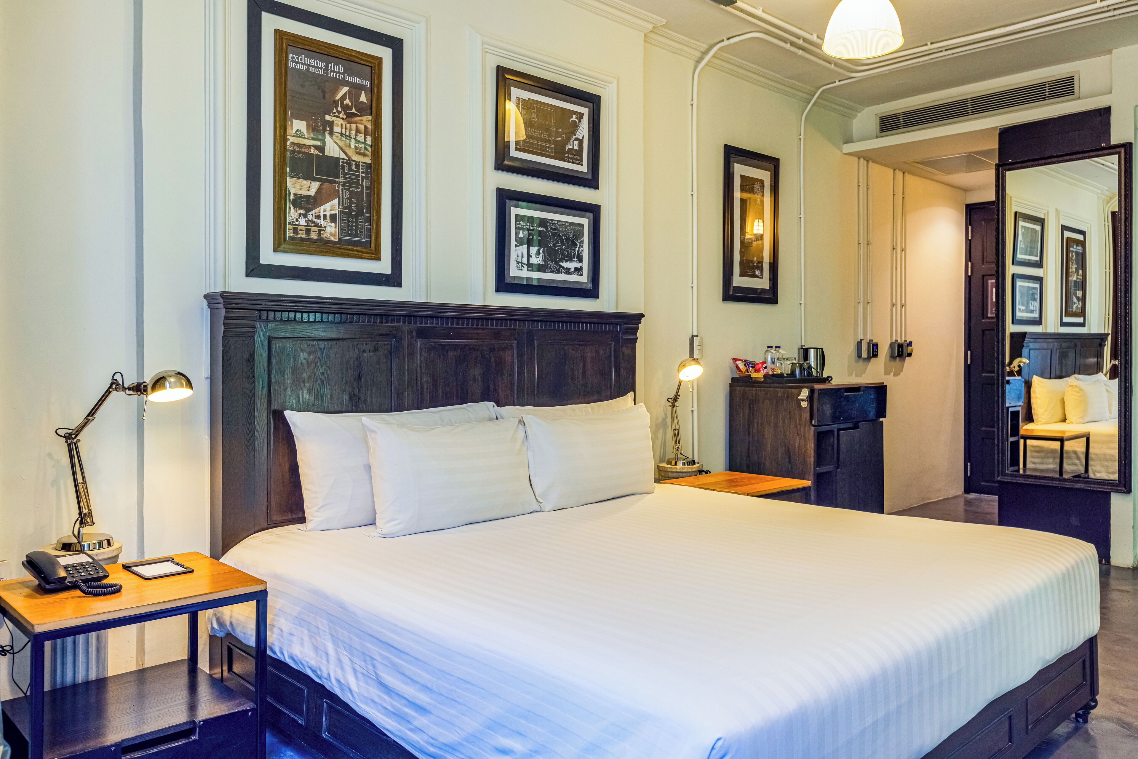 Una camera d'albergo ordinata con un letto grande, comodini, una scrivania e quadri appesi alle pareti.