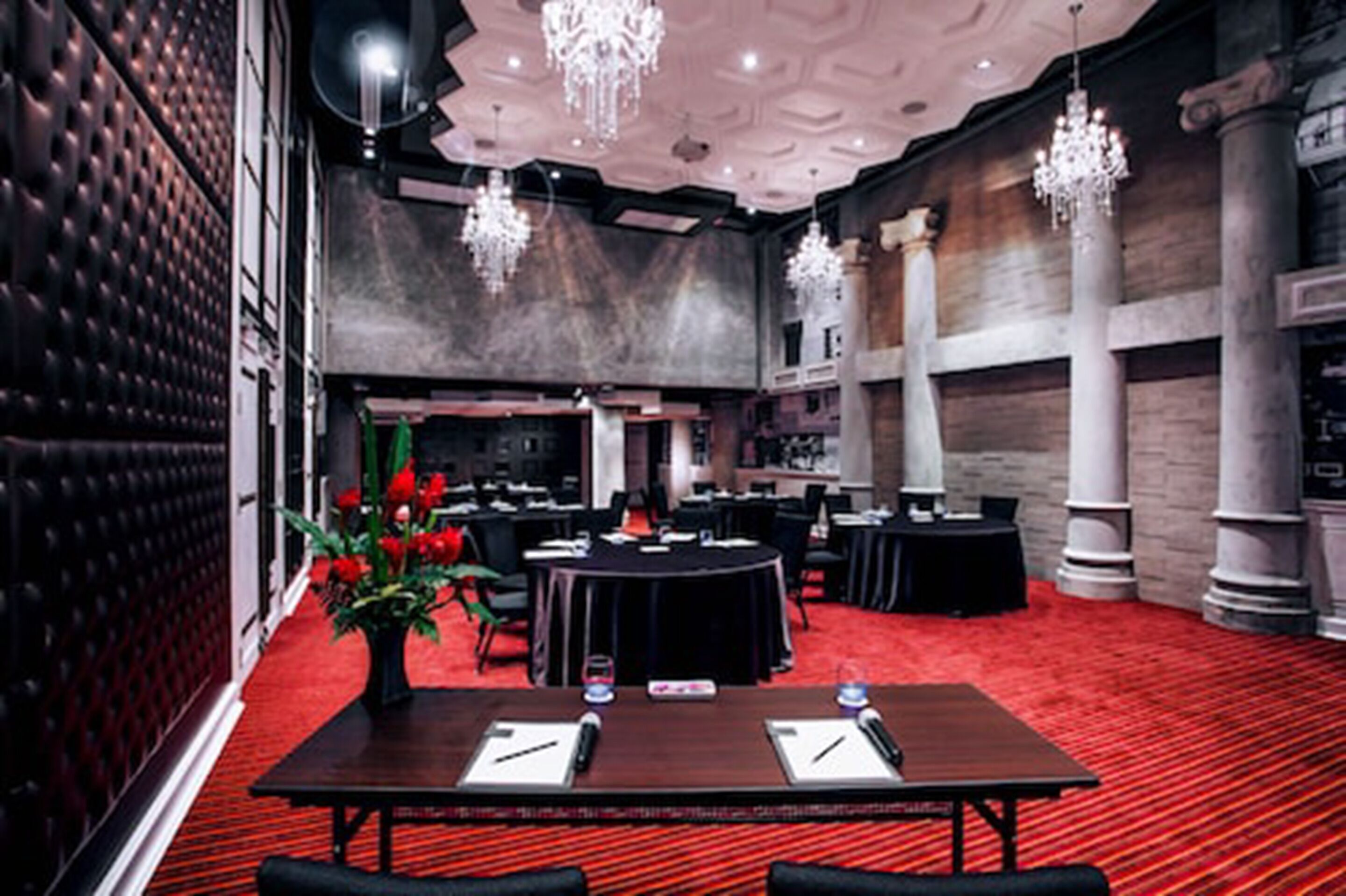 Un salón de conferencias con alfombra roja, mesas redondas y sillas negras.