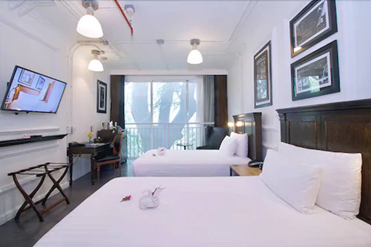 A hotel room with two beds, a desk, a chair, a TV, and framed pictures on the wall.