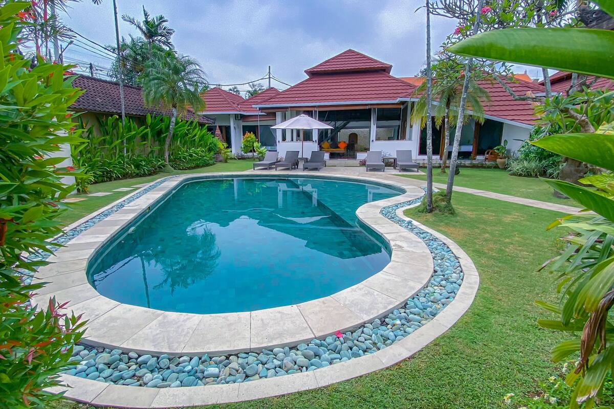 Uma piscina com borda curva, ladeada por um canteiro de pedras e um gramado bem cuidado.