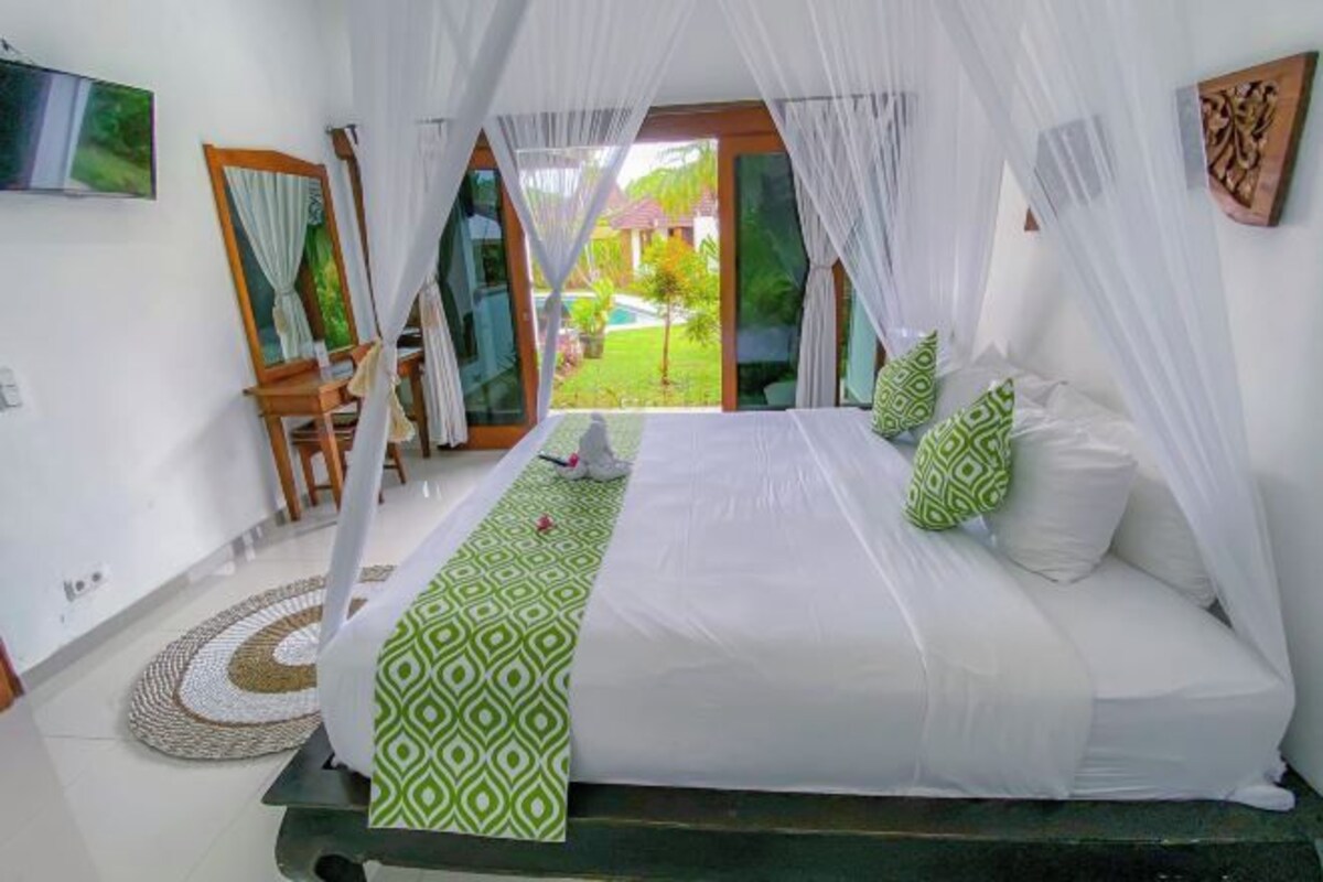 A bedroom with a bed, curtains, a view of the outdoors, a TV, and a chair.