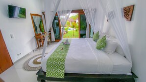 A bedroom with a bed, a desk, and a chair. There is a view of a garden through the window. - Dyana Villas (Seminyak)