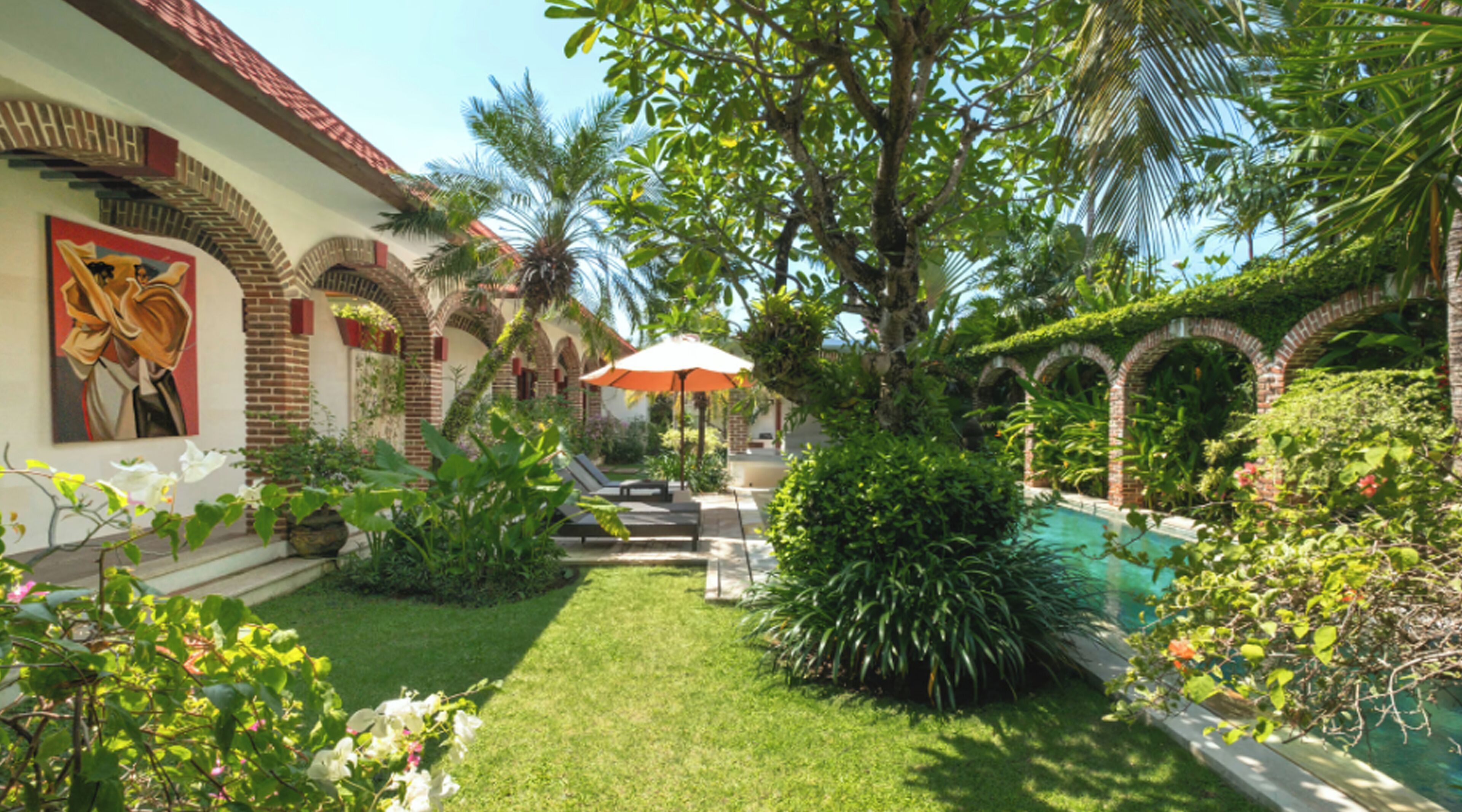 A lush garden with a swimming pool, palm trees, and a mural on the building.