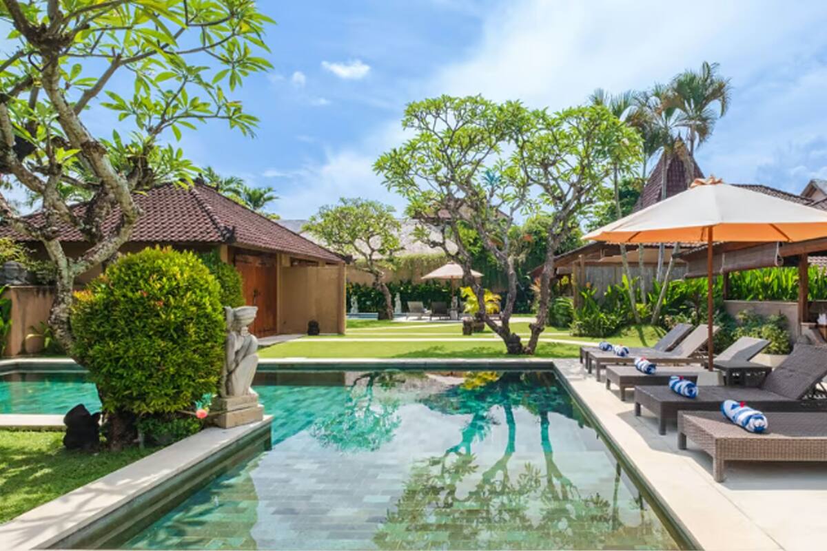 Uma área de piscina com espreguiçadeiras e guarda-sóis, rodeada por vegetação e arquitetura tradicional.