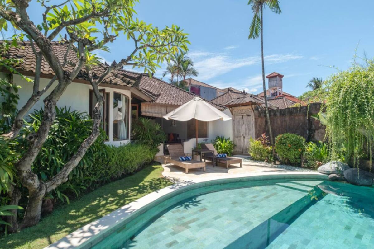Um imóvel residencial com piscina, varanda coberta com assentos e vegetação exuberante.