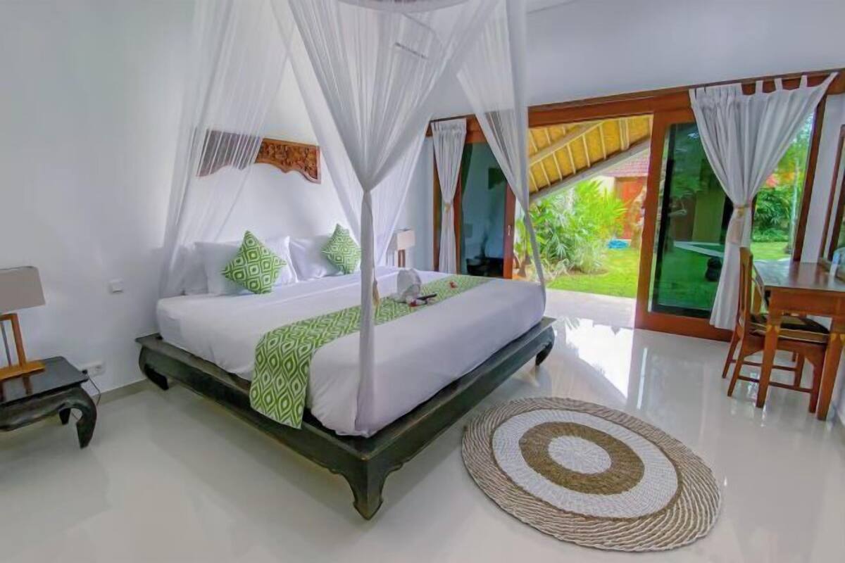 Quarto com cama, mesa de cabeceira, cadeira, tapete redondo e vista para o exterior.