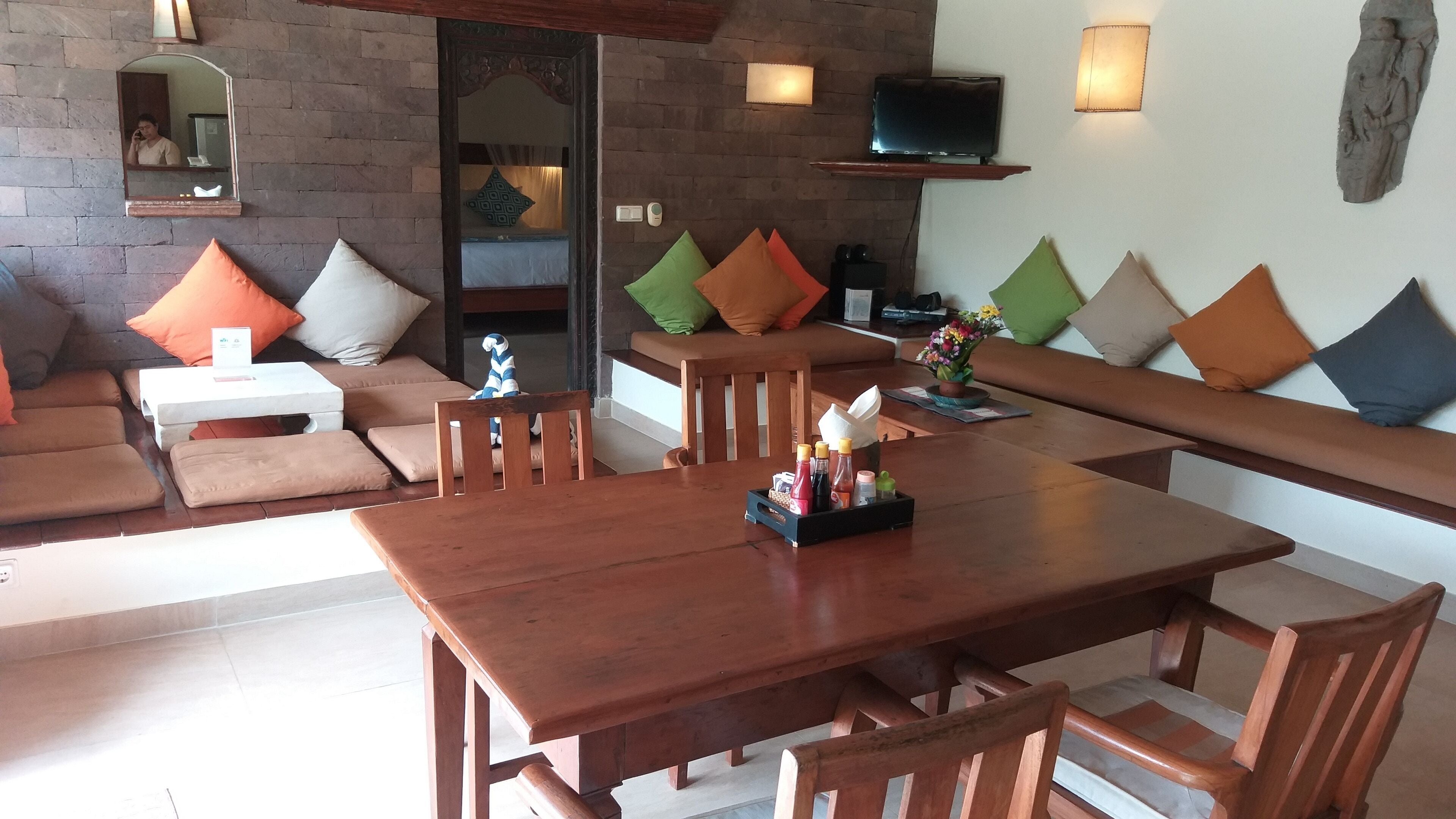 Una sala de estar acogedora con una mesa de comedor de madera, asientos acolchados y un televisor montado en la pared.
