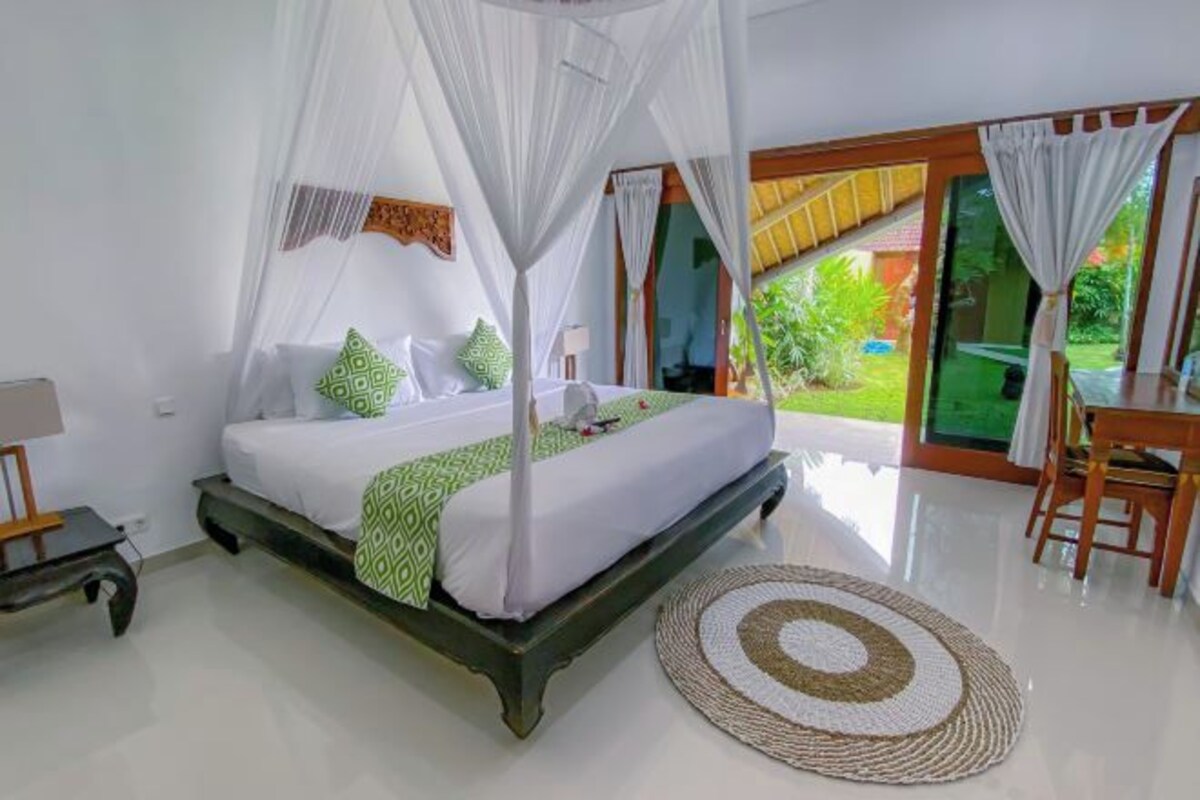 A bedroom with a bed, a bedside table, a chair, a round rug, and a view of the outdoors.