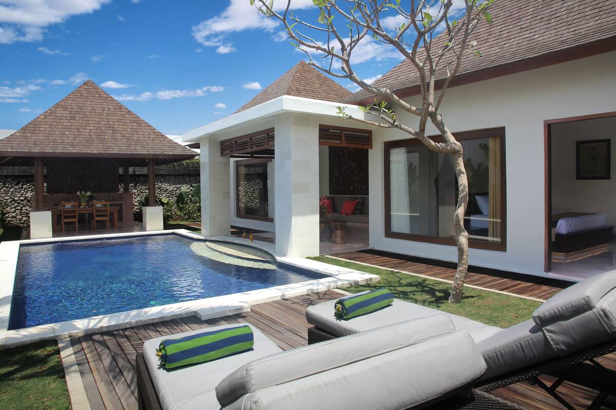 A modern outdoor pool area with lounge chairs and a covered seating area.