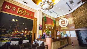 A hotel lobby with a reception desk, seating area, and a large wall mural of a cityscape. - Li Qing Hotel (Kaohsiung)