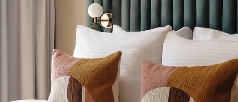 Cama bem arrumada com cabeceira estofada em verde, roupa de cama branca e duas almofadas estampadas.