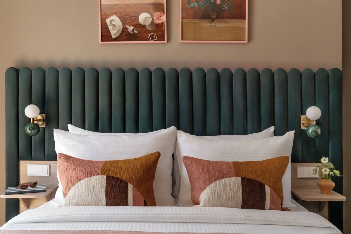 Una cama bien hecha con dos almohadas, una mesita de noche con una lámpara y un cuadro enmarcado en la pared.