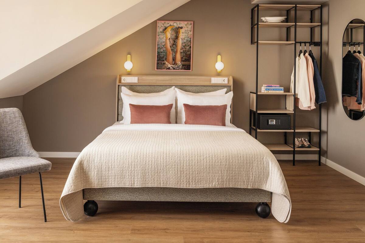 Un dormitorio con cama, una silla, un armario y un cuadro en la pared.