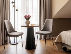 A modern hotel room with two grey upholstered chairs, a round table with a vase of flowers, and a bed with a quilted cover. - Numa Munich St Paul (Munich)