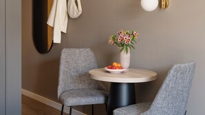 A modern room with a round table, two grey chairs, a vase with flowers, a bowl of fruit, a coat rack with coats, and a wall-mounted light fixture. - Numa Munich St Paul (Munich)