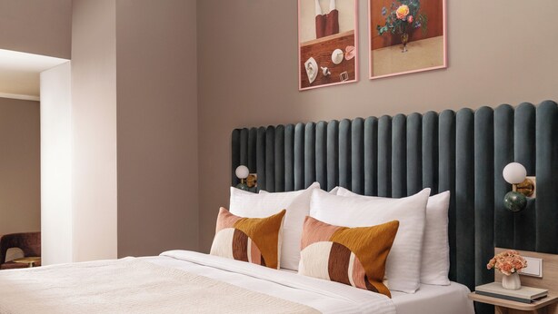 A modern bedroom with a bed, a nightstand, a wall-mounted lamp, and two framed pictures. - Numa Munich St Paul (Munich)