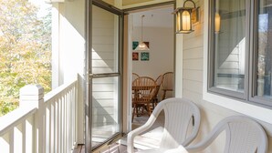 A porch with white chairs, a glass door, and a dining table with chairs. - Vantage Point Villas at Stratton Mountain Resort (Stratton)